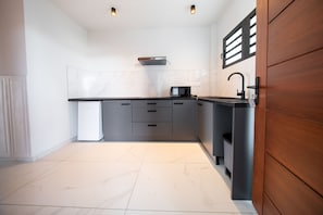 A modern kitchen with a black countertop, white tiles, and a wooden door.