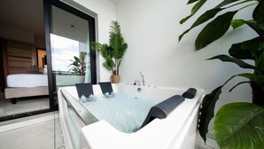 Une salle de bain moderne avec une grande baignoire, une plante en pot et une vue sur une chambre à coucher avec un lit et une fenêtre.