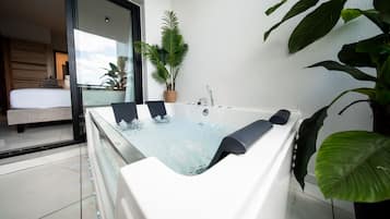 Une salle de bain moderne avec une grande baignoire, une plante en pot et une vue sur une chambre à coucher avec un lit et une fenêtre.