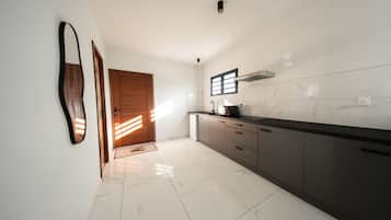 A modern kitchen with white marble tiles, dark cabinetry, and a wooden door.