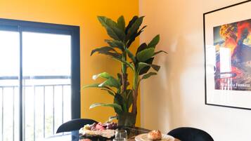 Een eetgedeelte met een tafel gedekt voor twee personen, een potplant en een ingelijste foto aan de muur.