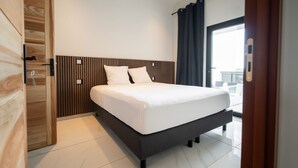 Une chambre d’hôtel moderne dotée d’un grand lit, d’une tête de lit en bois et offrant une vue sur la ville grâce à une grande fenêtre.