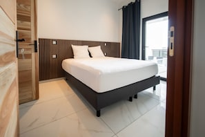 Una habitación de hotel moderna con una cama grande, un cabecero de madera y vistas de la ciudad a través de un ventanal.