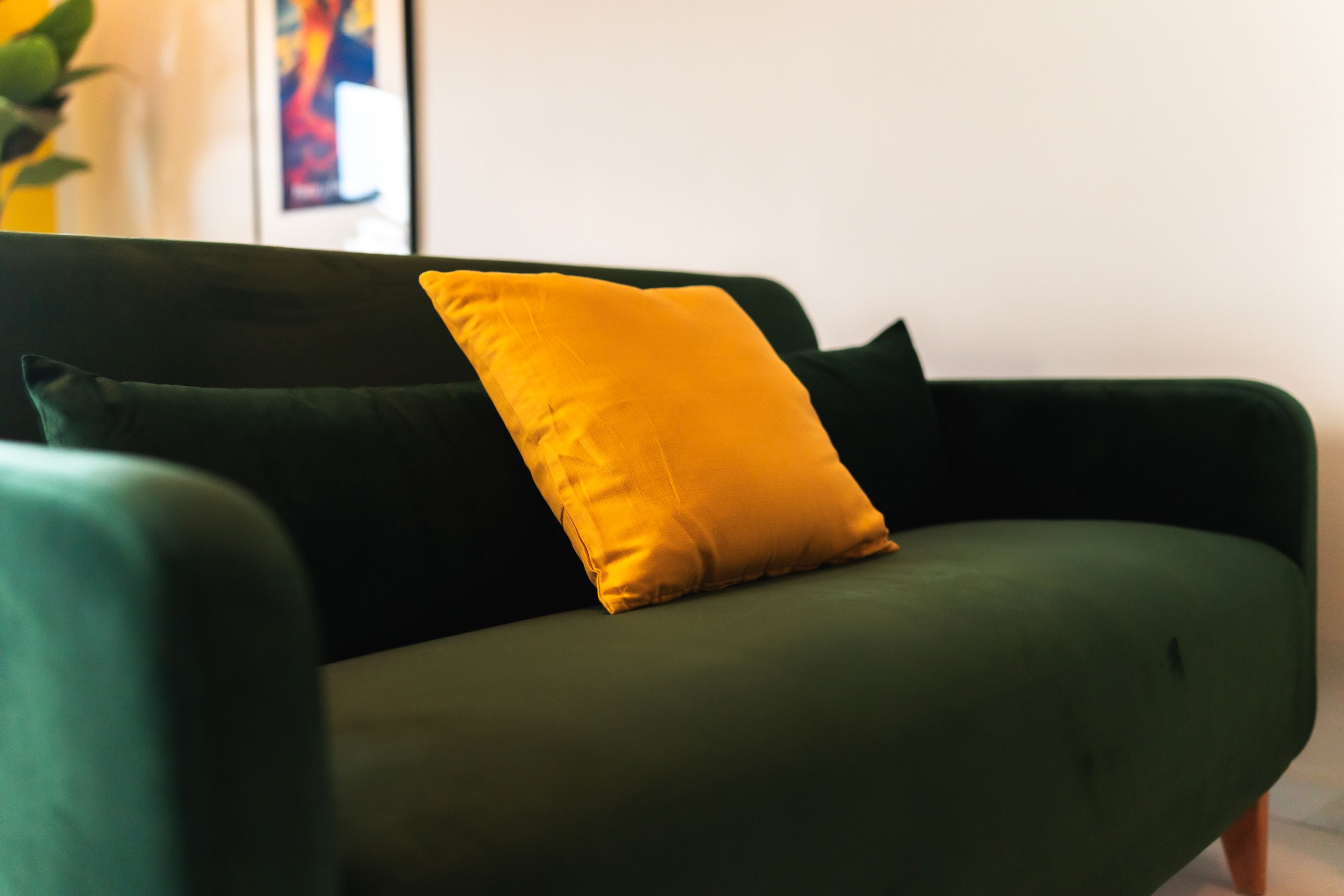A green sofa with a single yellow pillow.