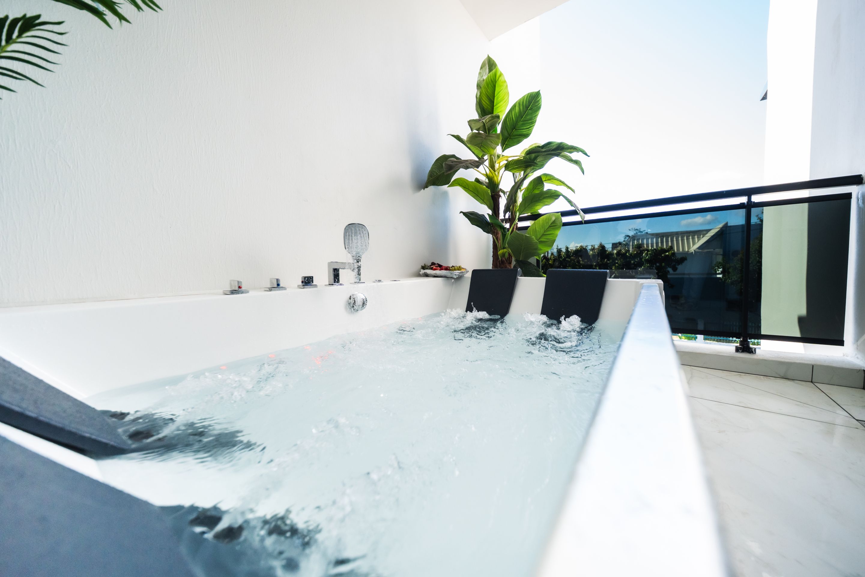 Un bain à remous intérieur moderne, offrant une vue dégagée sur le ciel et agrémenté d’une grande plante en pot.