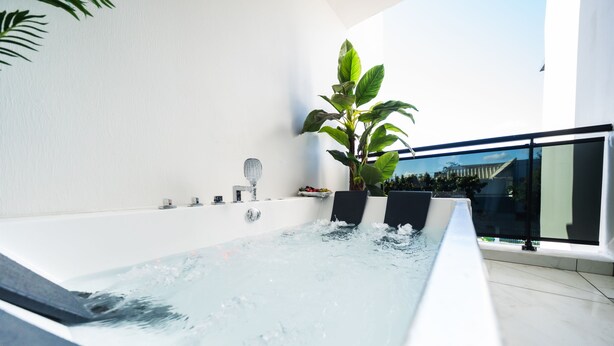 Un bain à remous intérieur moderne, offrant une vue dégagée sur le ciel et agrémenté d’une grande plante en pot.