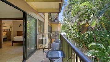 A balcony with a glass door leading to a bedroom, a small table with a cushion, and a chair.