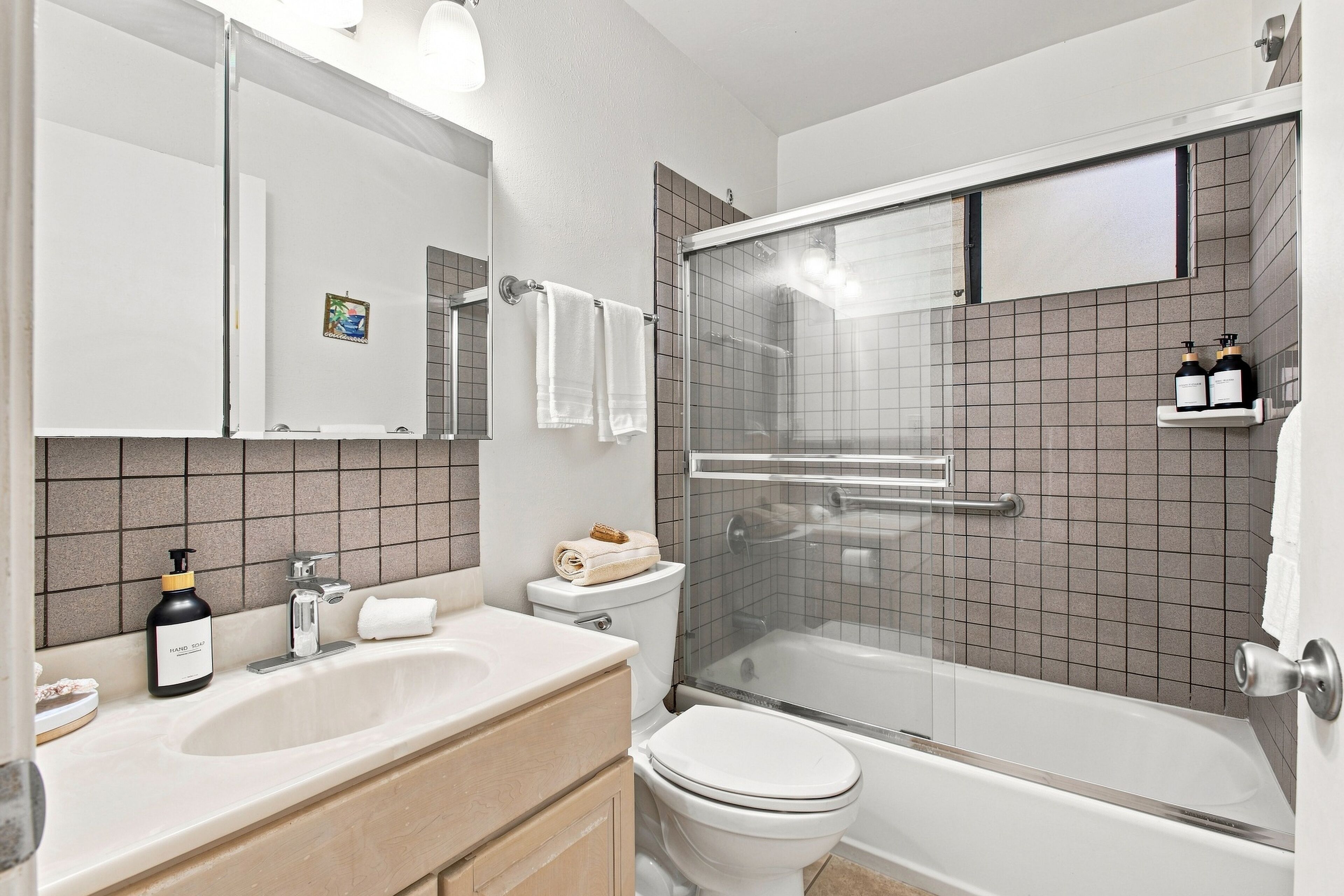 A modern bathroom with a glass-enclosed shower, a white toilet, a sink with a soap dispenser, and a mirror above the sink.