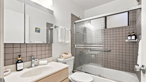 Un baño moderno con ducha envuelta en vidrio, inodoro blanco, lavamanos con dispensador de jabón y un espejo sobre el lavamanos.