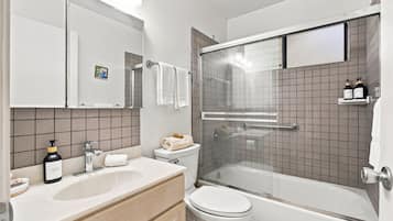 A modern bathroom with a glass-enclosed shower, a white toilet, a sink with a soap dispenser, and a mirror above the sink.