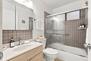 Ett modernt badrum med en dusch som är avskärmad med glasväggar, en vit toalett, ett handfat med en tvålpump och en spegel ovanför handfatet.