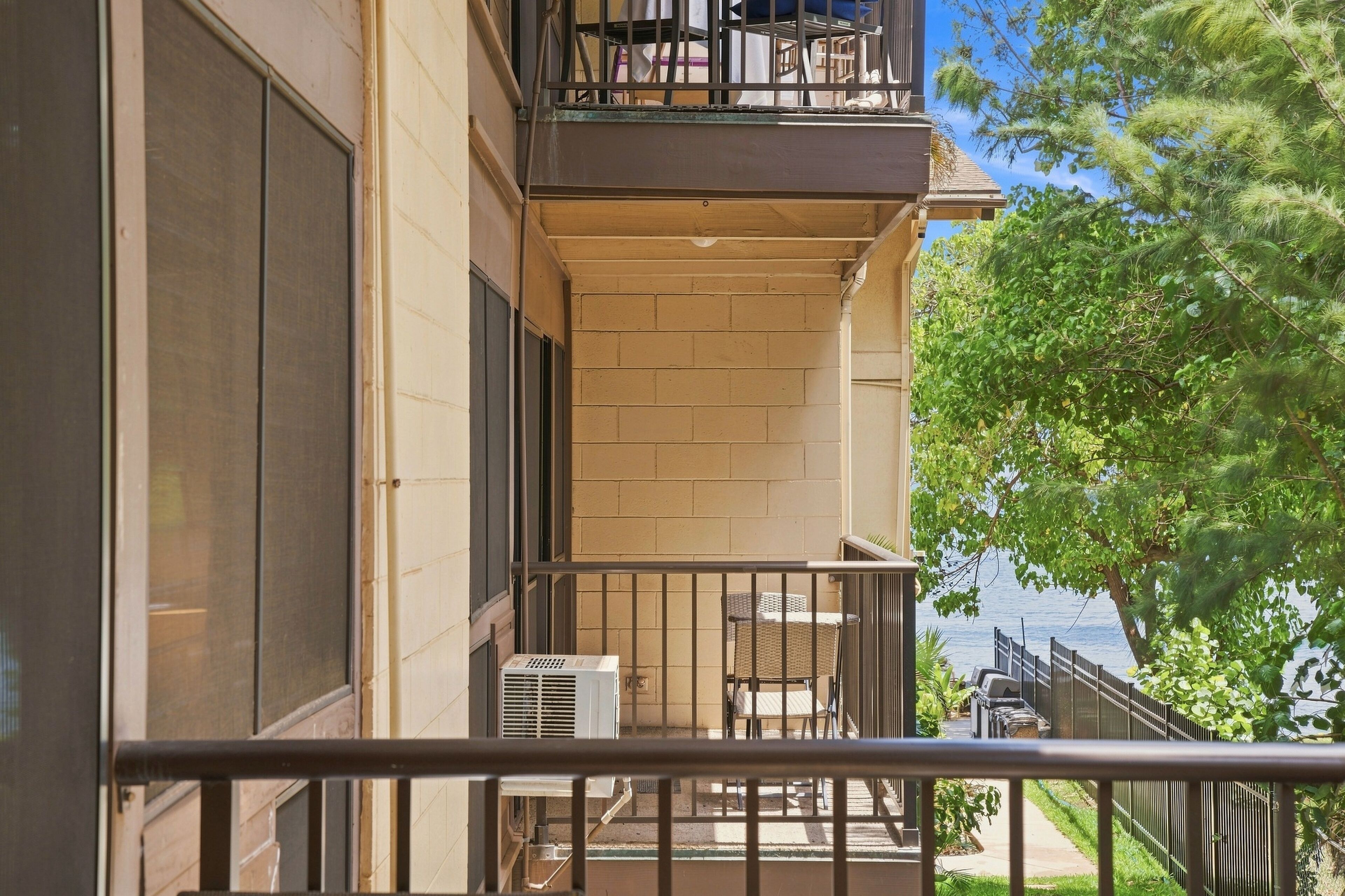 A balcony with a view of a body of water, a small outdoor seating area, and a building with a brick facade.