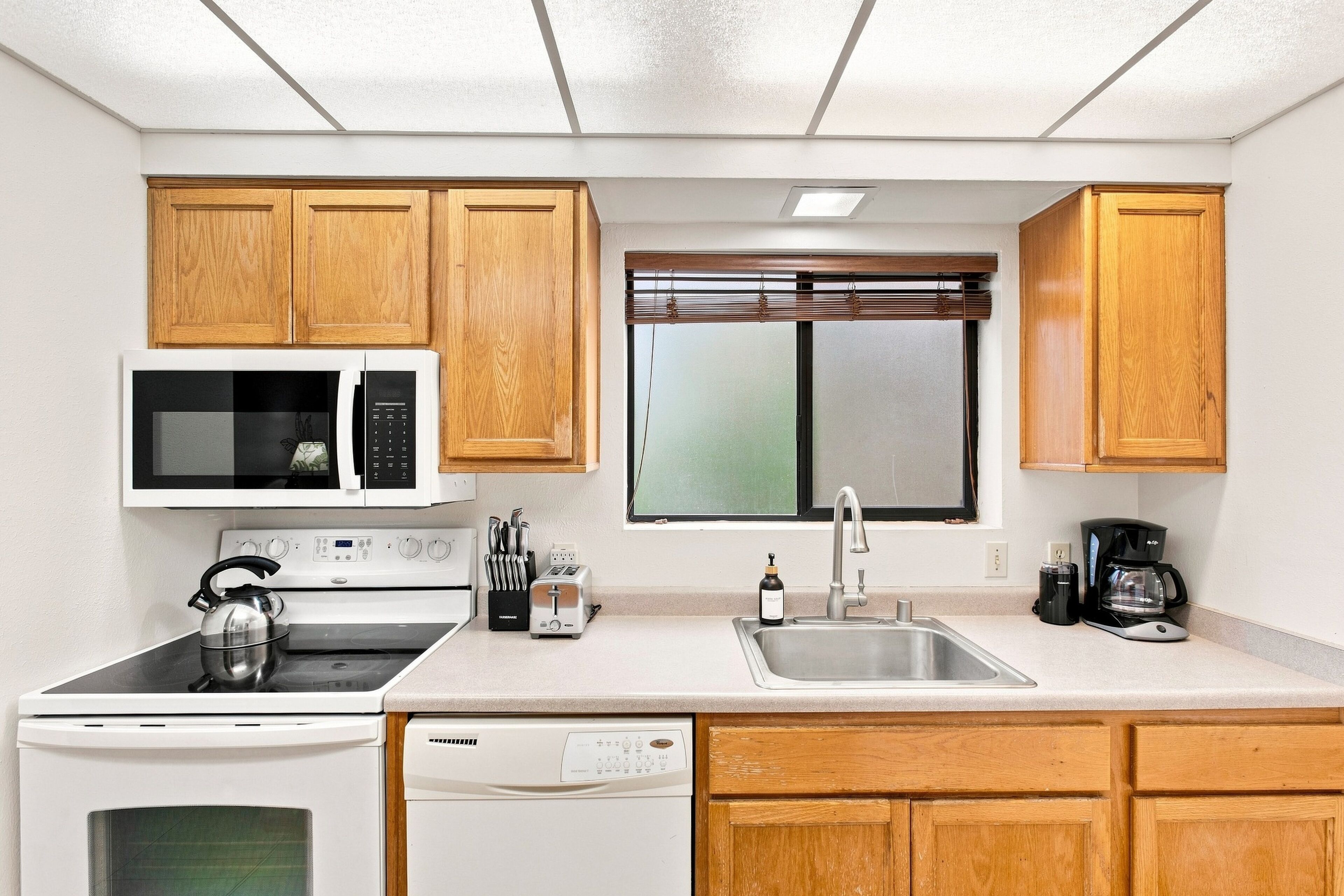 A compact kitchen with a microwave, stove, toaster, sink, and coffee maker.