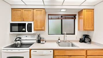 A compact kitchen with a microwave, stove, toaster, sink, and coffee maker.