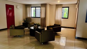 A hotel lobby with a reception desk, seating area, and a red door. - 1303  Nobre e Moderno com Garagem (Belém)