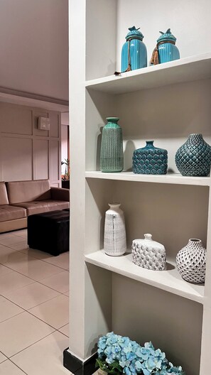 A room with a white shelf holding various ceramic vases, a brown sofa, and a black ottoman. - 1303  Nobre e Moderno com Garagem (Belém)