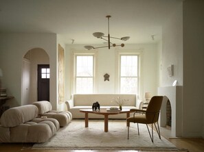 Un salon spacieux comprenant un canapé, une table basse et un fauteuil. On y trouve également une cheminée et une fenêtre donnant sur un beau paysage.