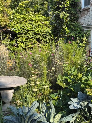 A garden with a round table, various plants, and a brick wall. - Mediterranean Retreat. Newly renovate 1,000 sqft. (Chicago)