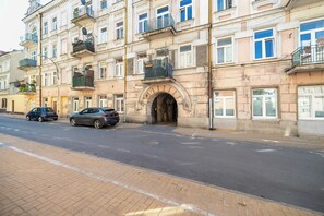 Un edificio a più piani con un ingresso centrale, balconi e auto parcheggiate sulla strada.