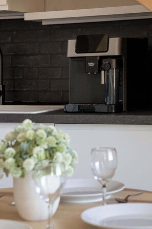 Una cucina con una macchina da caffè, una parete in mattoni e un tavolo da pranzo con un vaso e un bicchiere.