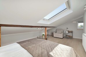 Une chambre avec un puits de lumière, un lit, une chaise, un bureau et un radiateur.