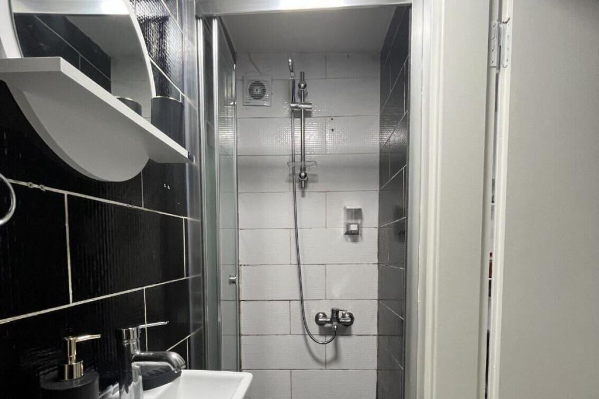 A bathroom with a white sink, black tiles, and a shower area.