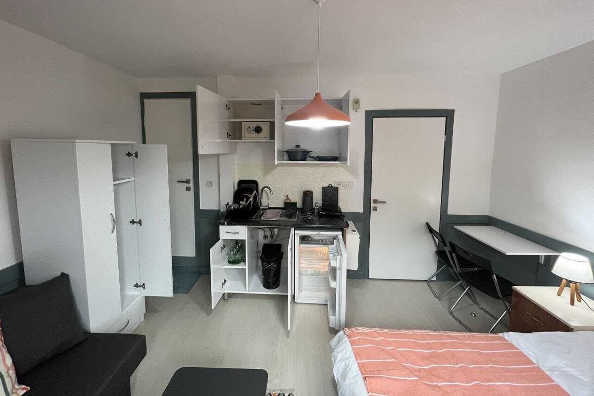 A compact room with a kitchenette, a bed, a desk, and a chair.