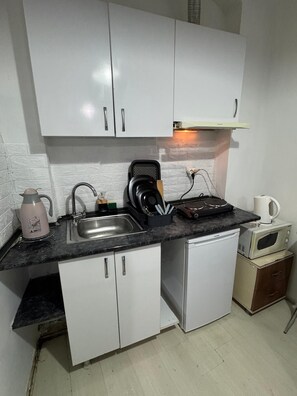 A compact kitchen with white cabinets, a black countertop, a kettle, a toaster, and a microwave. - amur (istanbul)