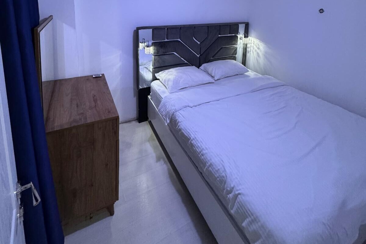 A bedroom with a bed, a bedside table, and a hanging light fixture.