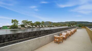 A rooftop terrace with a pool, lounge chairs, and a view of the mountains.