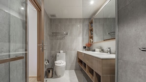 A modern bathroom with a glass shower enclosure, a wooden vanity with a mirror, and a toilet. - Seashore Beach Residences by NLA (Choeng Thale)