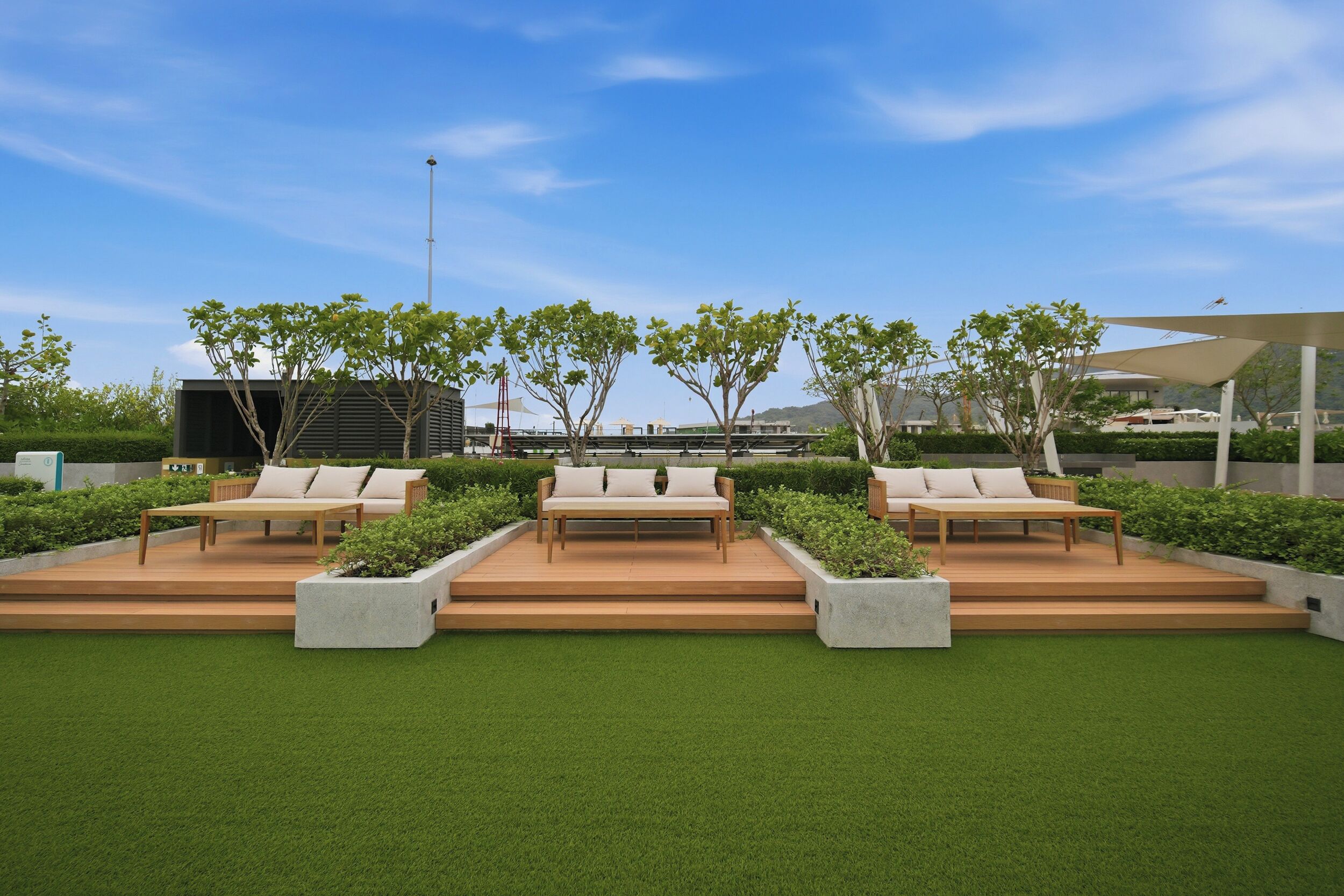 A rooftop garden with three wooden benches, surrounded by greenery and a clear sky.