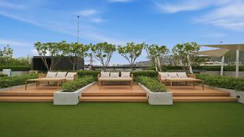 A rooftop garden with three wooden benches, surrounded by greenery and a clear sky.