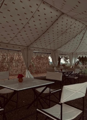 An indoor tent with tables and chairs, a patterned ceiling, and a straw wall. - Gulabbagh jawai  (Jawai Bandh)