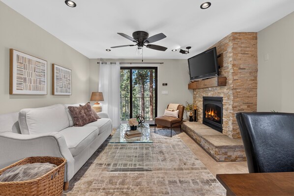 A modern living room with a fireplace, a sofa, a coffee table, and a television mounted on the wall. - Beaver Village Unit 624 2 bed remodeled, private deck w/forest views (Winter Park)