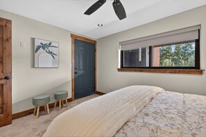 Une chambre à coucher avec un lit, une fenêtre avec des stores, une porte et un ventilateur de plafond.