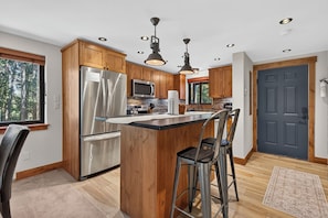 Een moderne keuken met houten kastjes, roestvrijstalen apparatuur en een centraal eiland met barkrukken.