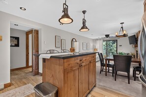 Een keuken met houten kasten, een centraal eiland, hanglampen en een eethoek met stoelen en een tafel.
