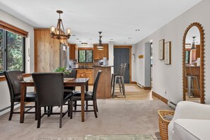 A modern kitchen with wooden cabinets, a dining area with a table and chairs, and a large window providing natural light. - Beaver Village Unit 624 2 bed remodeled, private deck w/forest views (Winter Park)