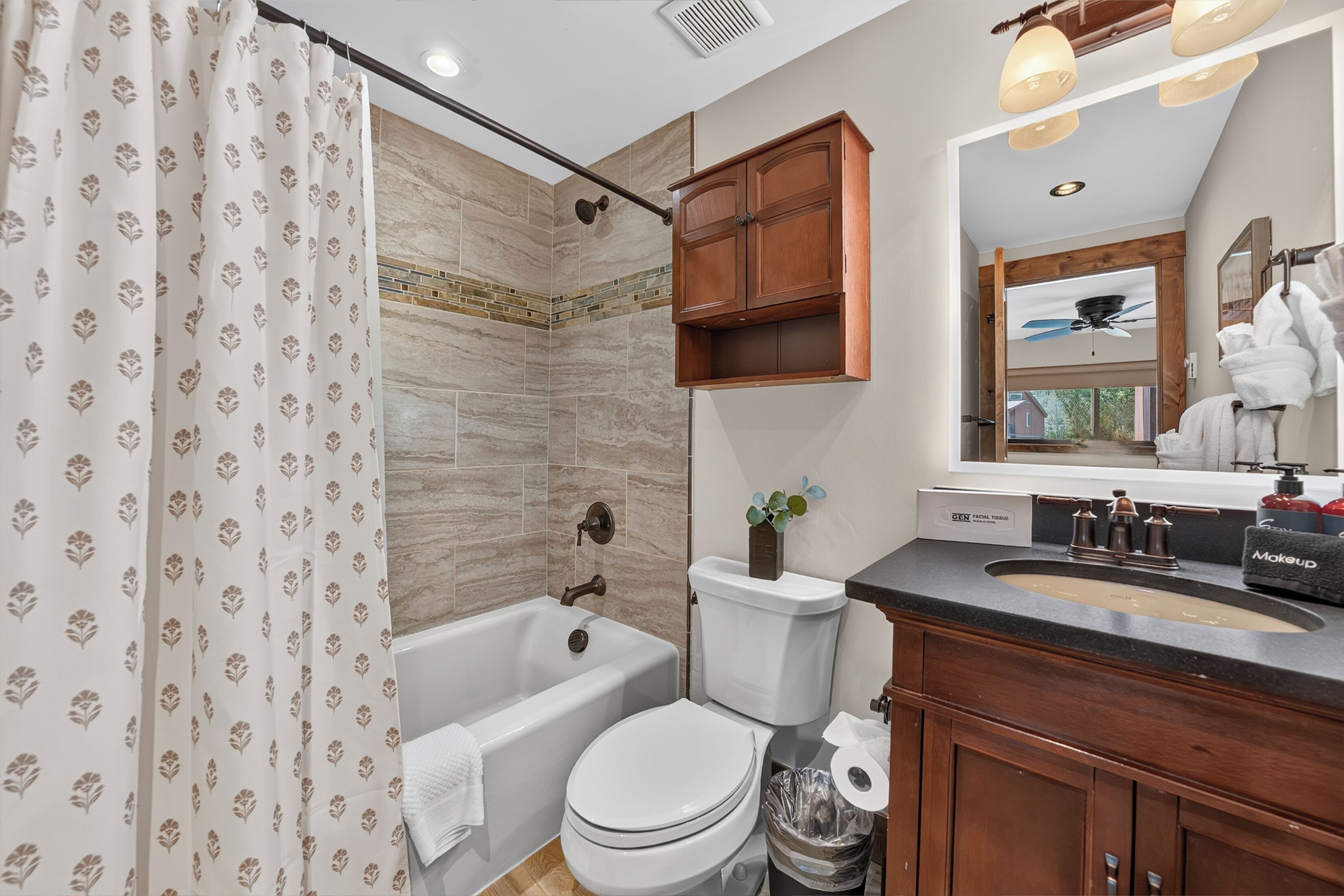 A bathroom with a shower, toilet, sink, and mirror.
