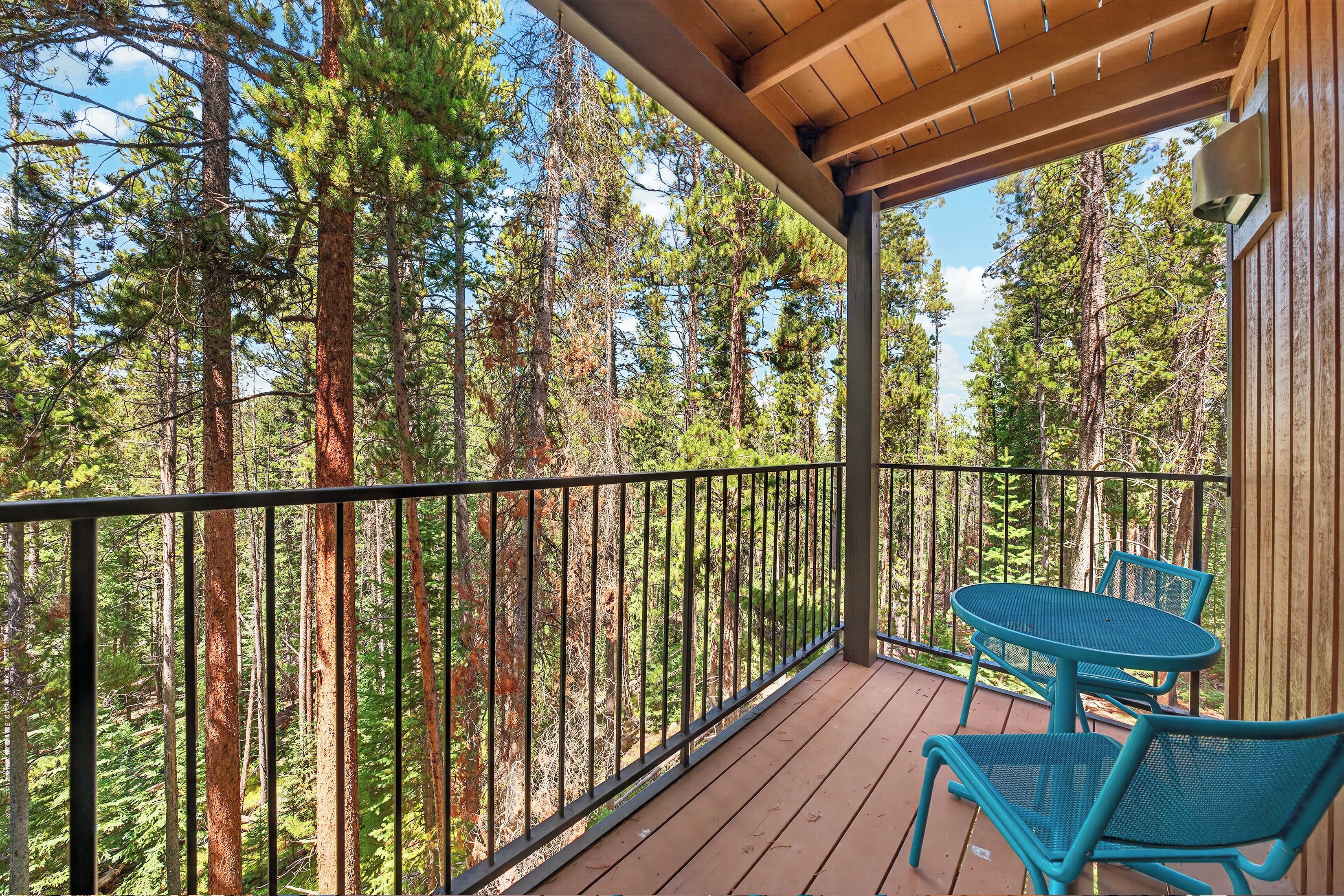 A wooden deck with a railing, overlooking a forest of tall trees.