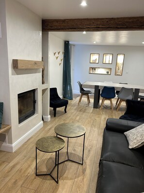 A modern living room with a fireplace, a dining area with a table and chairs, and a seating area with a sofa and two small tables. - The Refuge of the Six Valleys • House for 8 people, 4 bedrooms  • Wi-Fi• Near the Alps (Livet-et-Gavet)