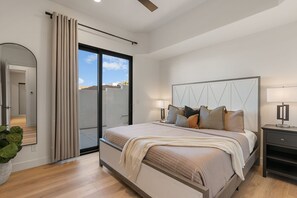 Ein modernes Schlafzimmer mit einem großen Bett, einem Nachttisch, einem Spiegel und einer Schiebeglastür zum Balkon.