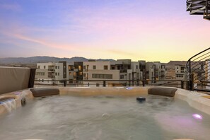 Een jacuzzi op een dak met uitzicht op moderne gebouwen en bergen op de achtergrond.