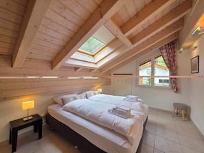 Ein Schlafzimmer mit einem großen Bett, einem Nachttisch, einer Lampe, einem Fenster mit Vorhängen und einem Dachfenster.