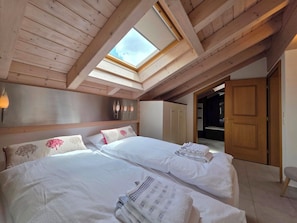 Ein Schlafzimmer mit zwei Betten, einem Oberlicht, Holzbalken, einem Kleiderschrank und einer Tür zu einem anderen Raum.