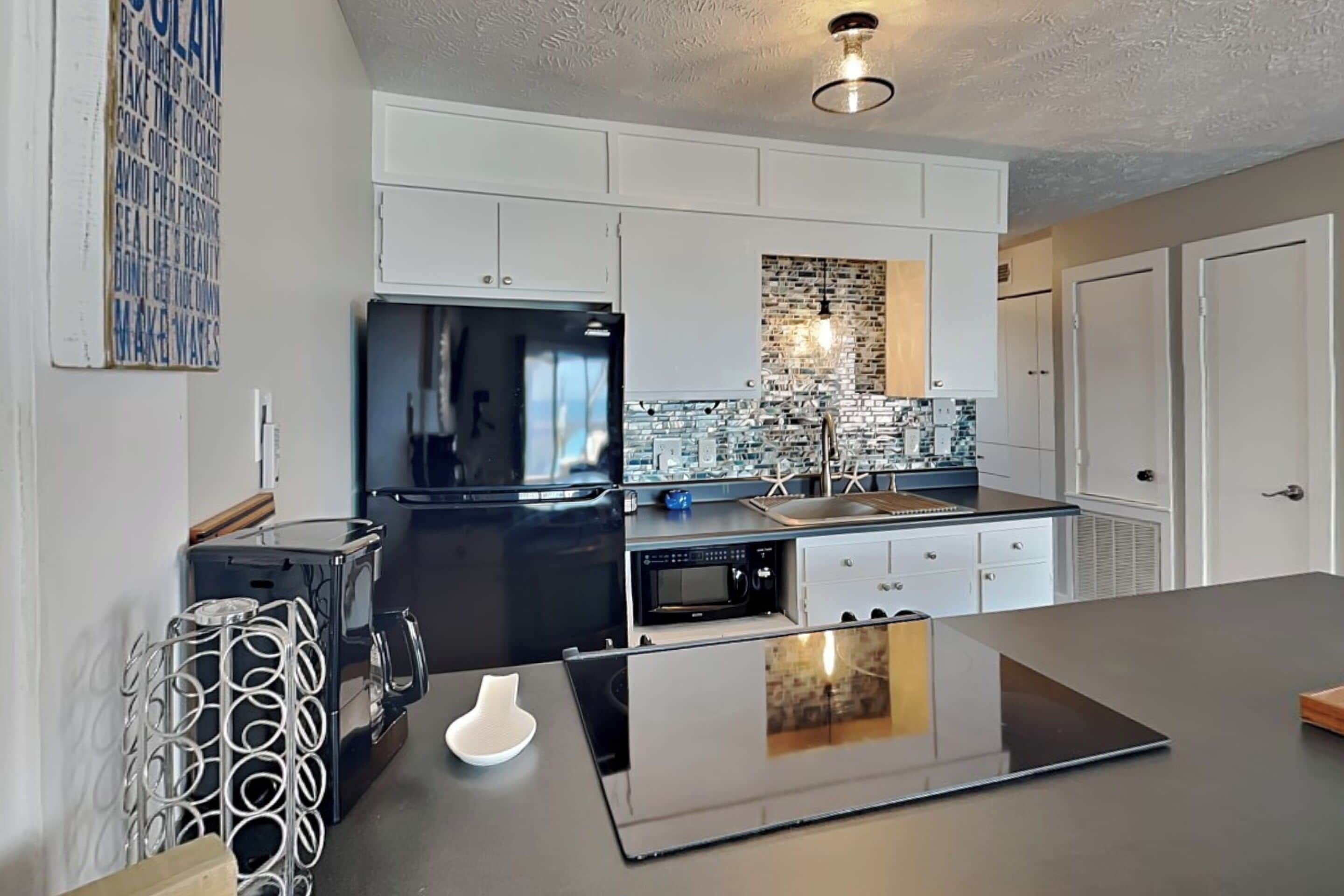 A modern kitchen with white cabinetry, a black refrigerator, a built-in oven, and a backsplash with a brick pattern.
