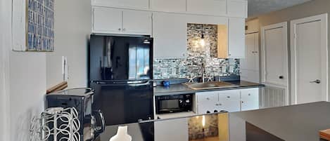 A modern kitchen with white cabinetry, a black refrigerator, a built-in oven, and a backsplash with a brick pattern.