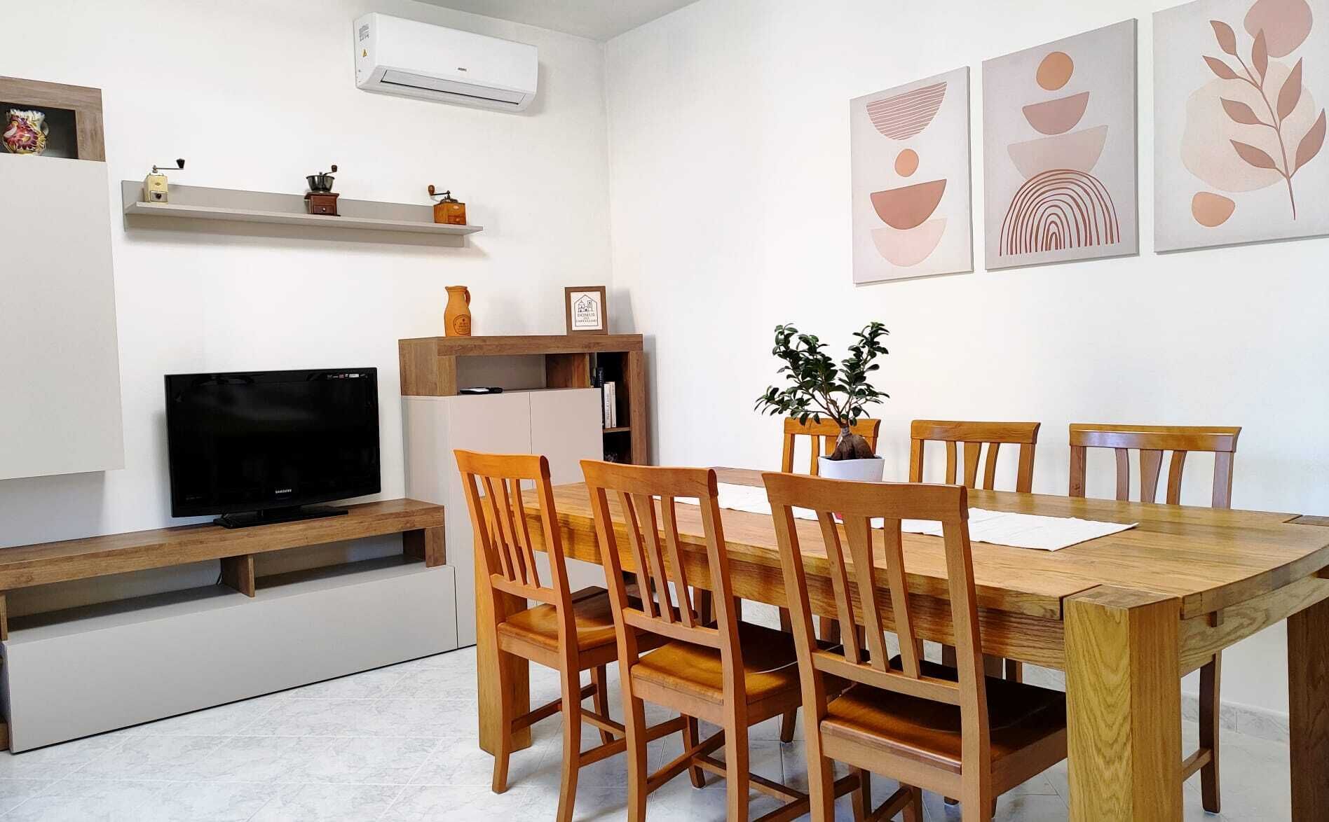 Un'area pranzo moderna con un tavolo e sedie in legno, una televisione su un mobile e un'opera d'arte appesa al muro.