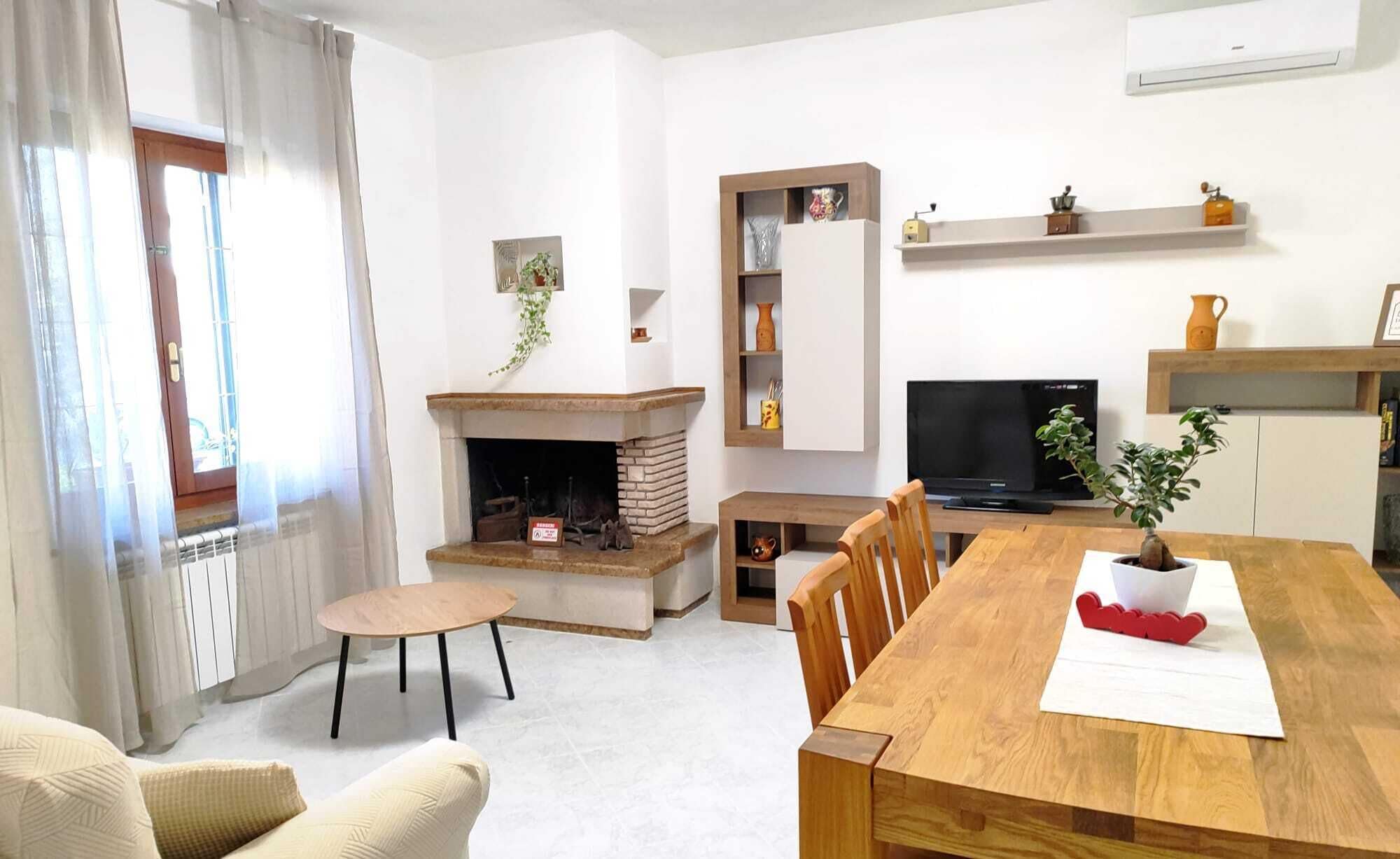 Ein Wohnzimmer mit Kamin, Fernseher, einem Esstisch mit Stühlen und einem Fenster mit Vorhängen.
